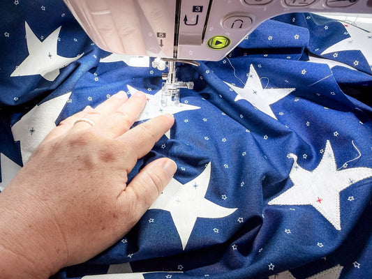 Sewing white star appliqués onto blue background fabric using a machine blanket stitch.